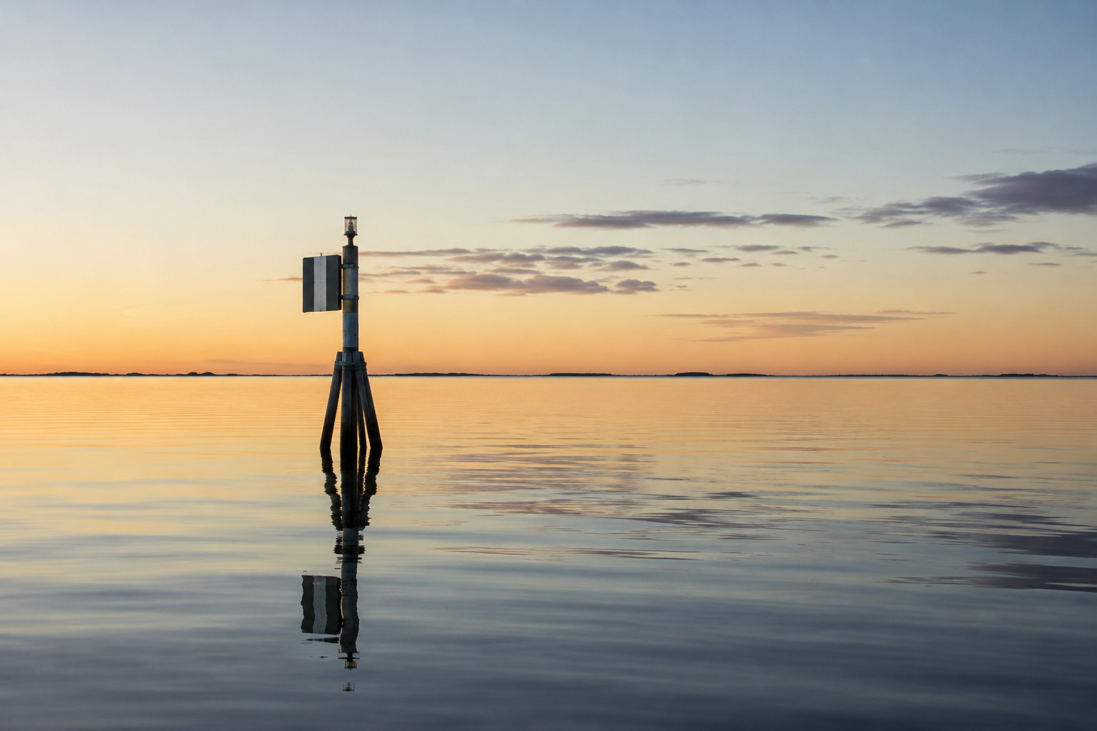 Calm Baltic water at dusk with a solitary navigation marker and soft horizon light
